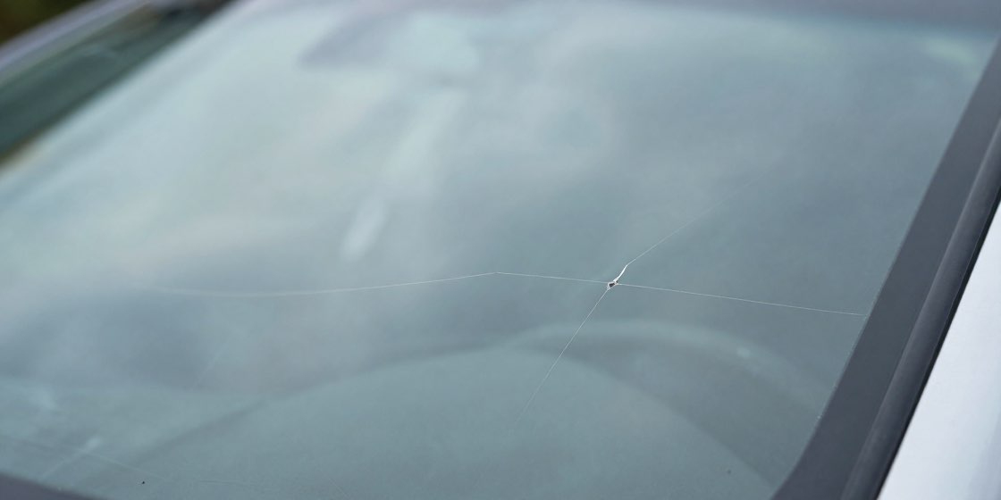 フロントガラスの小さな衝撃点から細いヒビが伸びている接写
